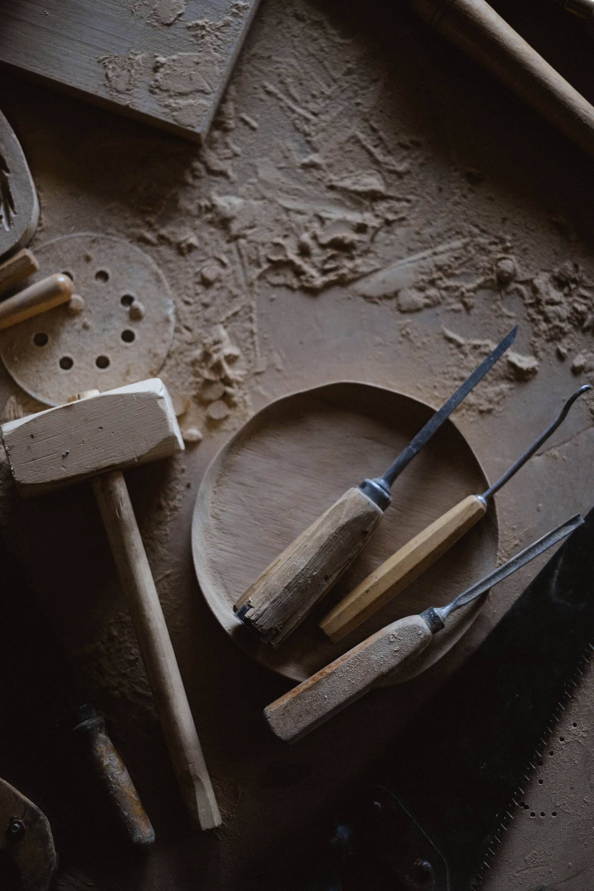 Top view of a joinery mallet and a set of chisels on a dusty wooden workbench with shavings