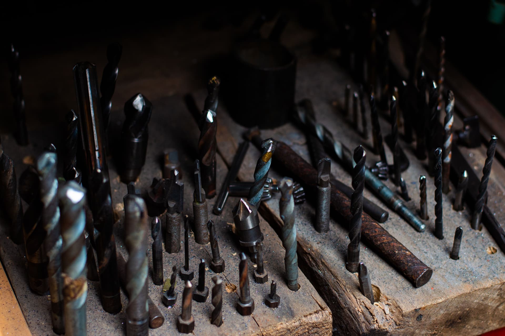 Close-up of many used drill bits standing in a battered wooden board